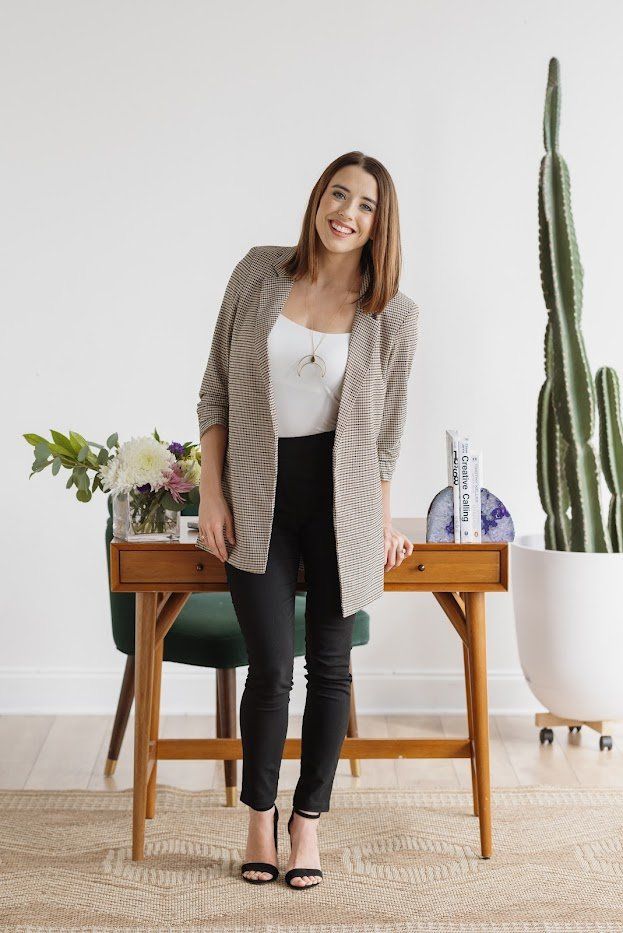 Emily Sledge, LCSW, standing beside a wooden desk with flowers and books in a warm office